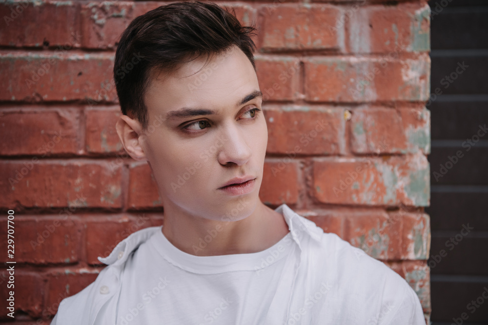 portrait of handsome young man looking away near brick wall
