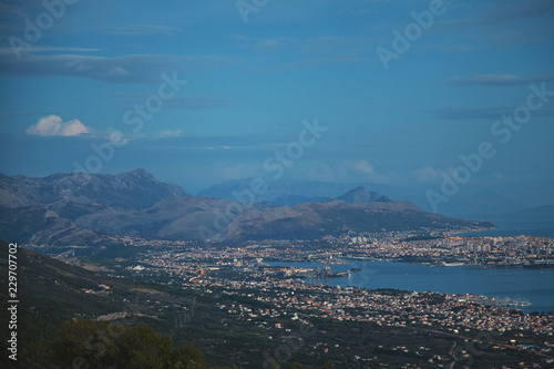 Small city by the sea surrounded by green trees and high hills view from top of mountain