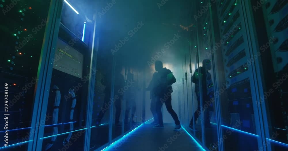 Wide, slow motion shot of a two hackers finishing hack and escaping a spark and smoke-filled corporate data center