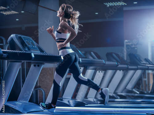Woman trains on a treadmill in the gym. Young fitness girl running on treadmill machine. Sports exercises for weight loss.