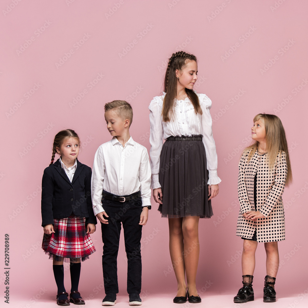 Cute smiling happy stylish children on pink background. Beautiful stylish teen girls and boy standing together and posing at studio. Classic style. Kids fashion and emotions concept. Cute smiling happy stylish children on pink background. Beautiful stylish teen girls and boy standing together and posing at studio. Classic style. Kids fashion and emotions concept.