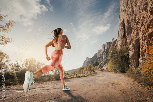 Young woman running on a mountain road in the beautiful nature. Girl runner in sneakers jogging workout outdoors. Weight loss concept. Healthy lifestyle.