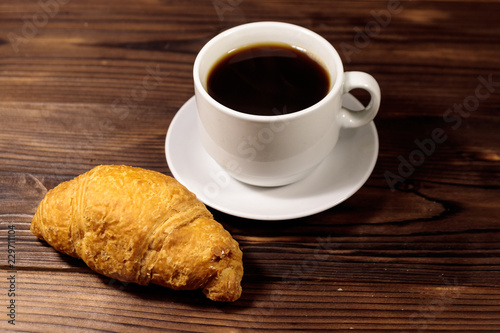 Cup of coffee and fresh croissant on wooden table