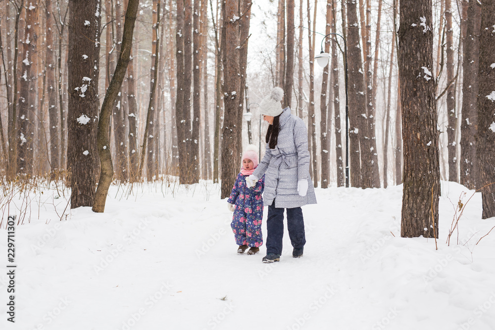 Winter, childhood and people concept - mother is walking with her little daughter in snowy forest