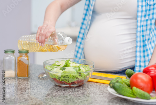 Close up pregnant woman in kitchen making a salad