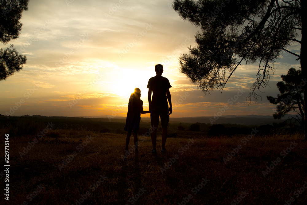 Backlight of a father and his daughter holding hands in a pine forest at sunset