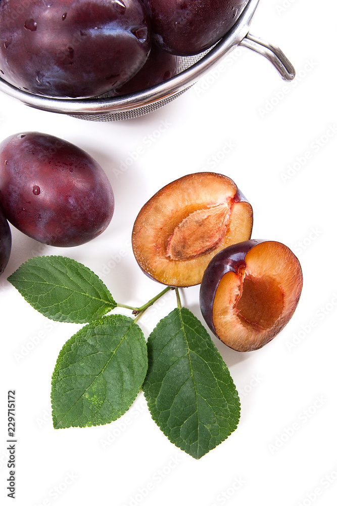 Obraz premium Steel colander with ripe plums, whole and half ripe plums with leaf isolated on a white background..