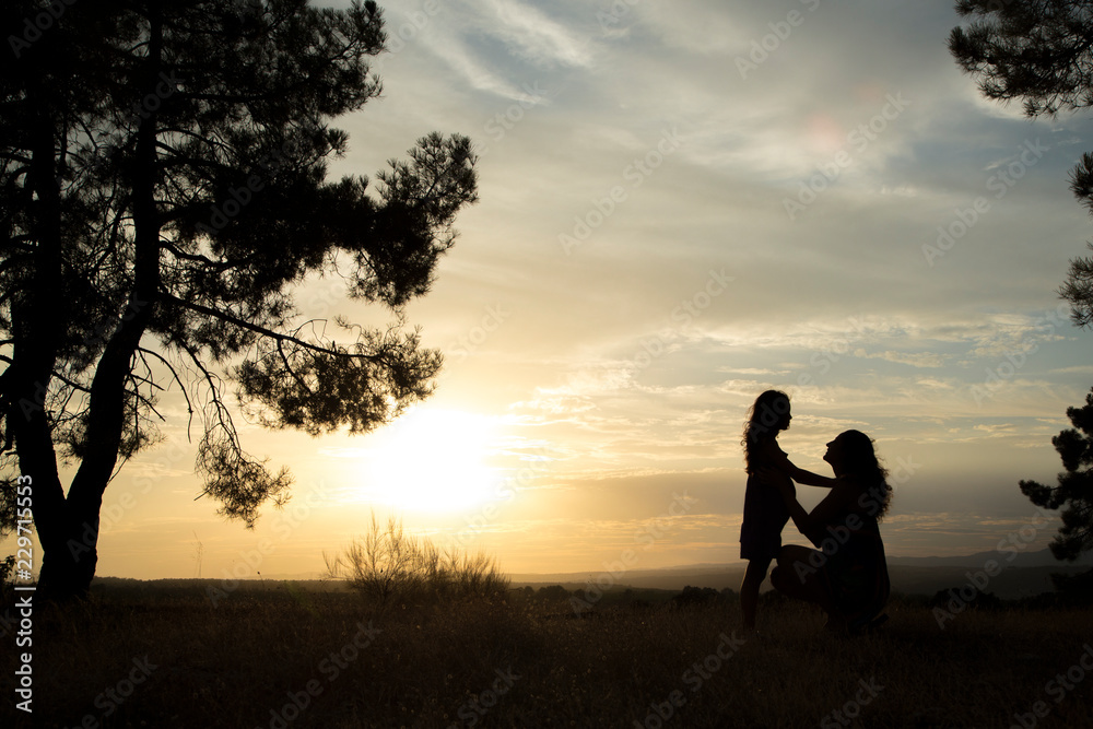 Backlight of a mother and daughter in a pine forest with yellow sky sunrise and sunset