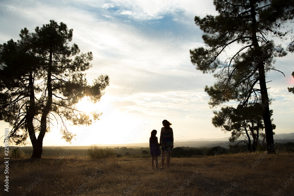 Backlight of a mother and daughter in a pine forest with yellow sky sunrise and sunset