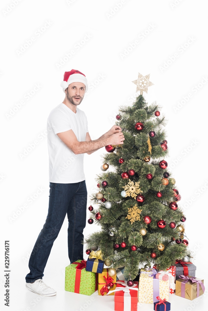 young man in red santa claus hat decorating christmas tree isolated on white young man in red santa claus hat decorating christmas tree isolated on white