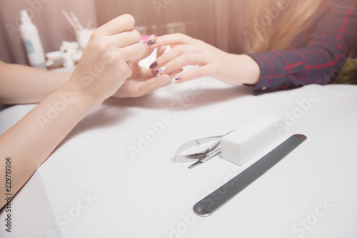 Manicure at beauty salon. Applying gel coating to girl with long hair. Close-up  warm lighting. Focus on tools