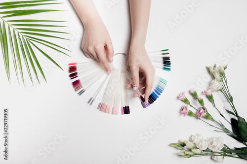 Beautiful photo of woman's hands with palette colors gel varnishes. Fashion care, nude manicure. Near palm green leaf and light pink flowers.