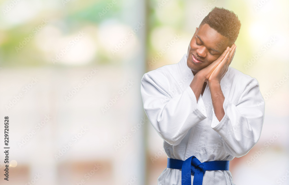 Young african american man over isolated background wearing kimono sleeping tired dreaming and posing with hands together while smiling with closed eyes. Young african american man over isolated background wearing kimono sleeping tired dreaming and posing with hands together while smiling with closed eyes.