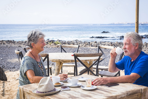 Fotografia Retired mature couple enjoying a beautiful sunny day at the beach drinking coffee and cappuccino together