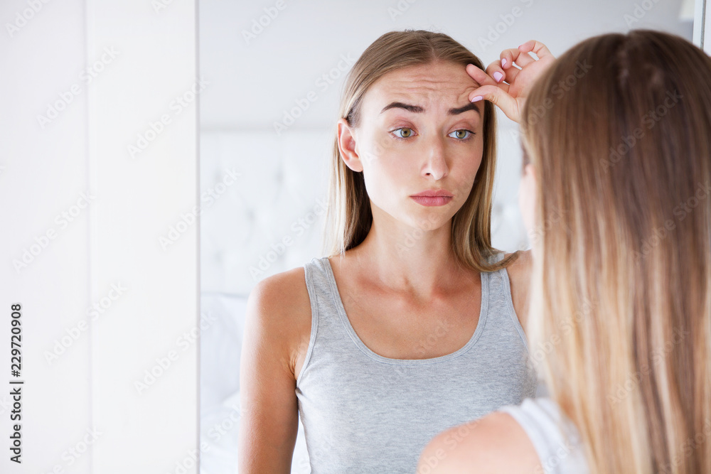 sexy woman touching her forehead while looking in the mirror in light room, beauty concept,wrinkles sexy woman touching her forehead while looking in the mirror in light room, beauty concept,wrinkles