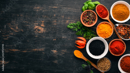 Fototapeta Naklejka Na Ścianę i Meble -  A set of spices and herbs. Indian cuisine. Pepper, salt, paprika, basil, turmeric. On a black wooden chalkboard. Top view. Free copy space.