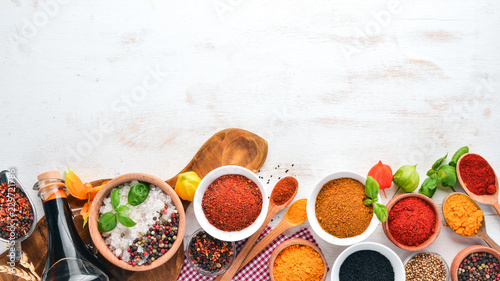 Fototapeta Naklejka Na Ścianę i Meble -  A set of Spices and herbs on a white wooden table. Basil, pepper, saffron, spices. Indian traditional cuisine. Top view. Free copy space.