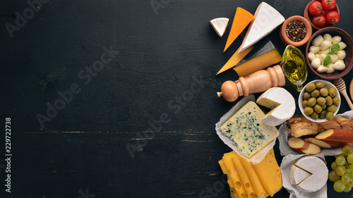 A large set of cheeses. Mozzarella, blue cheese, brie cheese, maasdam. Top view. On a black wooden background. Free space for your text.