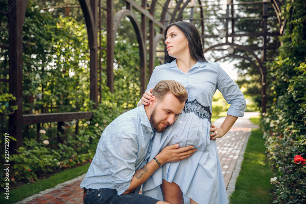 couple pregnant in the spring in the flowered garden, a man listening to stomach of pregnant couple pregnant in the spring in the flowered garden, a man listening to stomach of pregnant