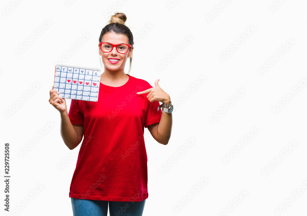 Young beautiful woman holding menstruation calendar over isolated background with surprise face pointing finger to himself