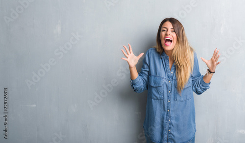 Young adult woman over grunge grey wall wearing denim outfit celebrating crazy and amazed for success with arms raised and open eyes screaming excited. Winner concept