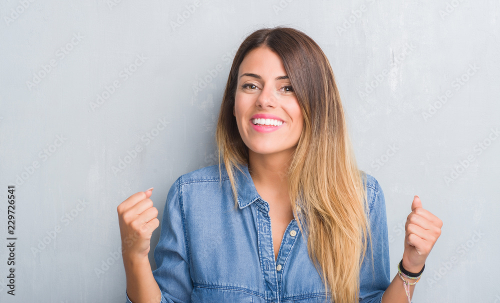 Young adult woman over grey grunge wall wearing denim outfit screaming proud and celebrating victory and success very excited, cheering emotion Young adult woman over grey grunge wall wearing denim outfit screaming proud and celebrating victory and success very excited, cheering emotion