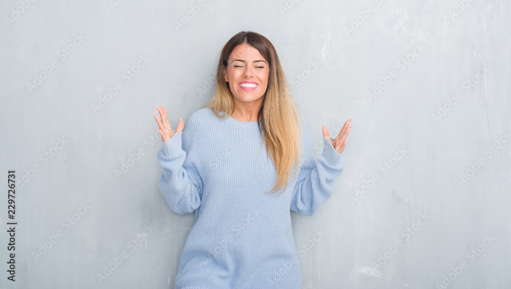 Young adult woman over grey grunge wall wearing winter outfit celebrating mad and crazy for success with arms raised and closed eyes screaming excited. Winner concept Young adult woman over grey grunge wall wearing winter outfit celebrating mad and crazy for success with arms raised and closed eyes screaming excited. Winner concept