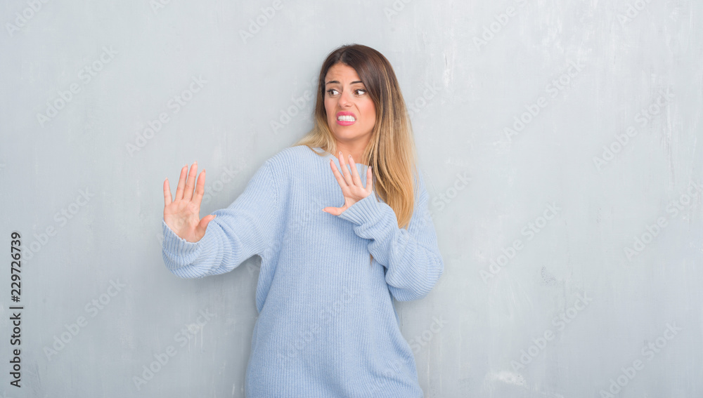 Young adult woman over grey grunge wall wearing winter outfit afraid and terrified with fear expression stop gesture with hands, shouting in shock. Panic concept. Young adult woman over grey grunge wall wearing winter outfit afraid and terrified with fear expression stop gesture with hands, shouting in shock. Panic concept.