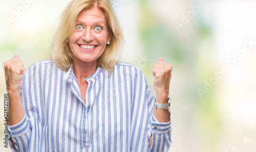 Middle age blonde business woman over isolated background celebrating surprised and amazed for success with arms raised and open eyes. Winner concept. © Krakenimages.com