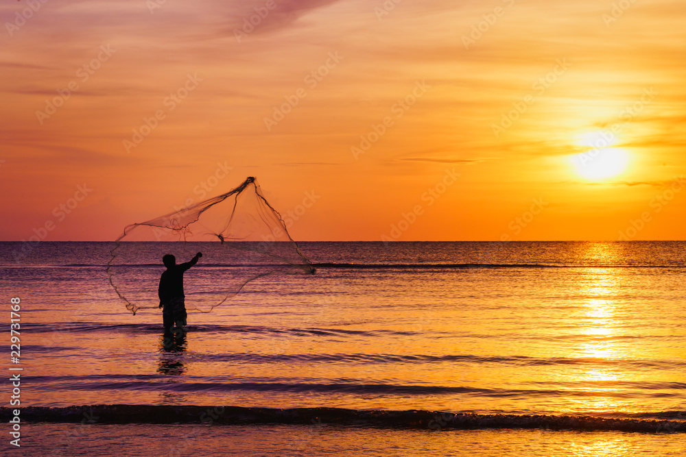 Silhouette of fisherman throwing fishing net in morning at tropical sea at  beautiful sunrise, twilight sky background. Stock Photo