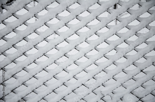 Texture of snow on the fencing net. Metal wire mesh covered with snow in winter.