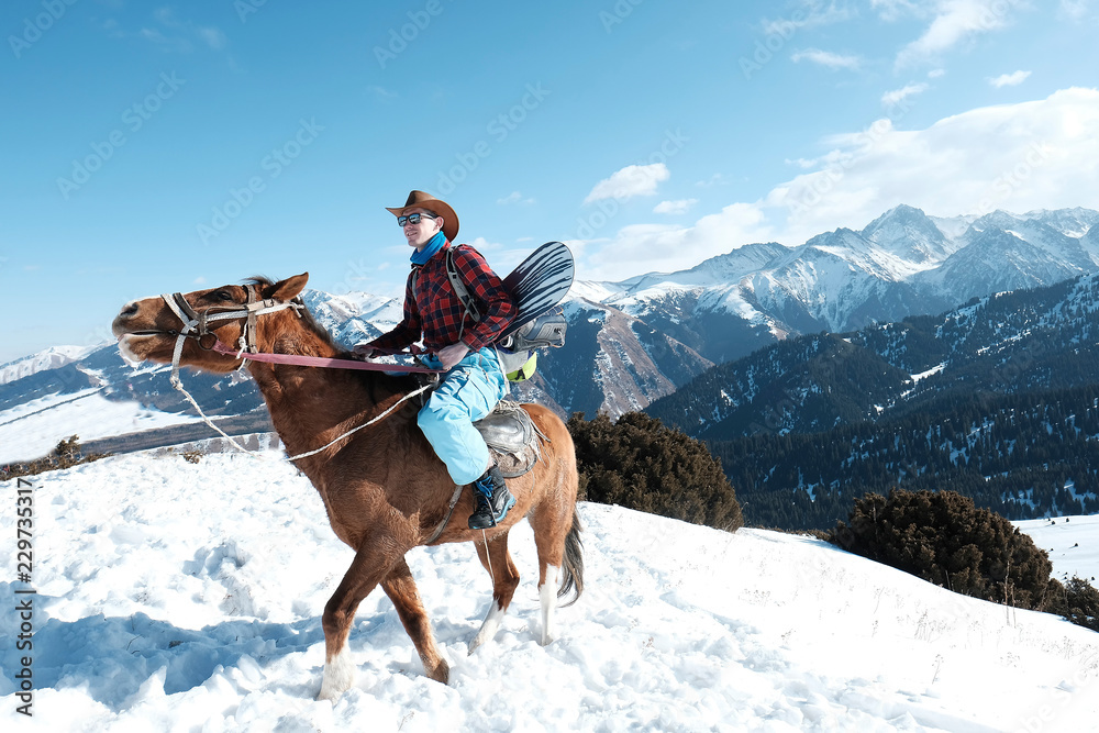 A man in a cowboy hat riding a horse in the snow. Winter. the mountains.