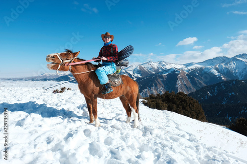 Snowboarder on a horse. Freeride. A man in a cowboy hat riding a horse in the snow. Winter. the mountains.