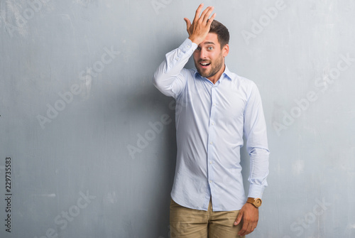 Handsome young business man over grey grunge wall wearing elegant shirt surprised with hand on head for mistake, remember error. Forgot, bad memory concept.