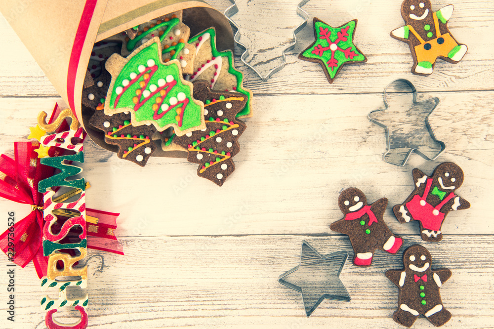 Obraz premium Beautiful Christmas composition and decoration with baked Christmas gingerbread cookies in paper bag on light wooden background, flat lay, top view, copy space (text space)