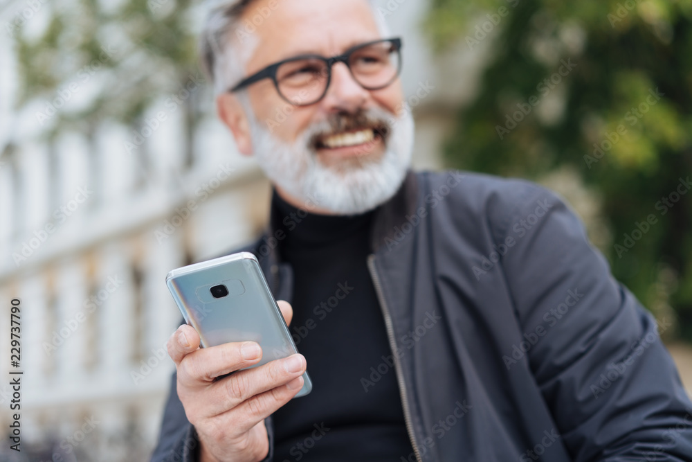 Smiling senior bearded man holding a mobile phone