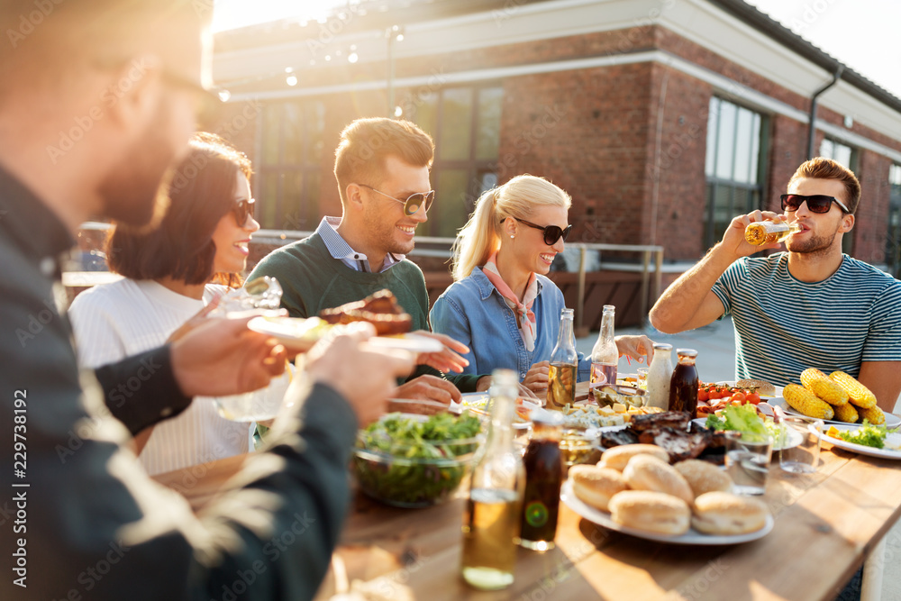 leisure and people concept - happy friends eating and drinking at barbecue party on rooftop leisure and people concept - happy friends eating and drinking at barbecue party on rooftop