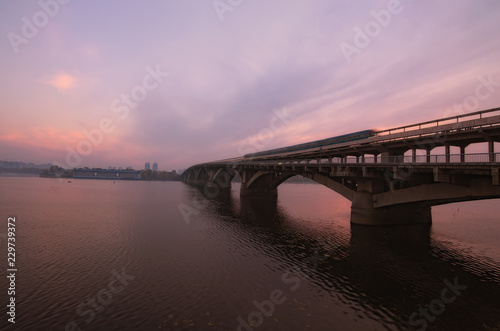 Merto Bridge with old underground train over Dnipro River. Scenic autumn landscape during sunrise. Colorful vibrant sky reflected in the water. Selective focus with wide angle lens. Kyiv, Ukraine