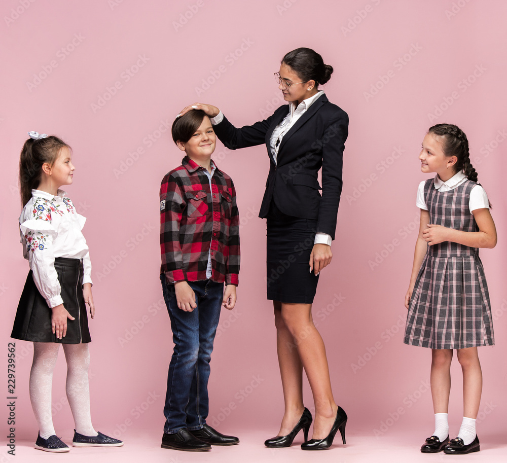 Cute smiling happy stylish children and female teacher on pink background. Beautiful stylish teen girls and boy standing together and posing at studio. Classic style. Kids fashion and emotions concept Cute smiling happy stylish children and female teacher on pink background. Beautiful stylish teen girls and boy standing together and posing at studio. Classic style. Kids fashion and emotions concept
