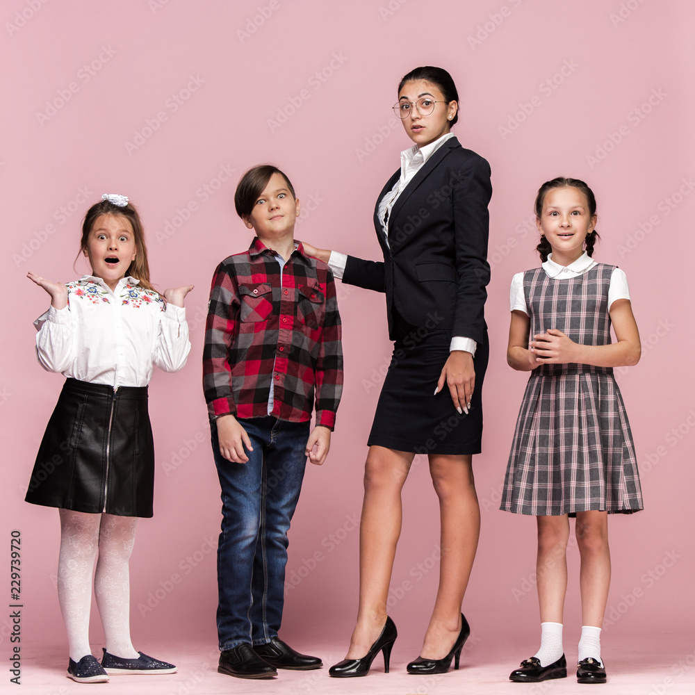 Cute smiling happy stylish children and female teacher on pink background. Beautiful stylish teen girls and boy standing together and posing at studio. Classic style. Kids fashion and emotions concept Cute smiling happy stylish children and female teacher on pink background. Beautiful stylish teen girls and boy standing together and posing at studio. Classic style. Kids fashion and emotions concept