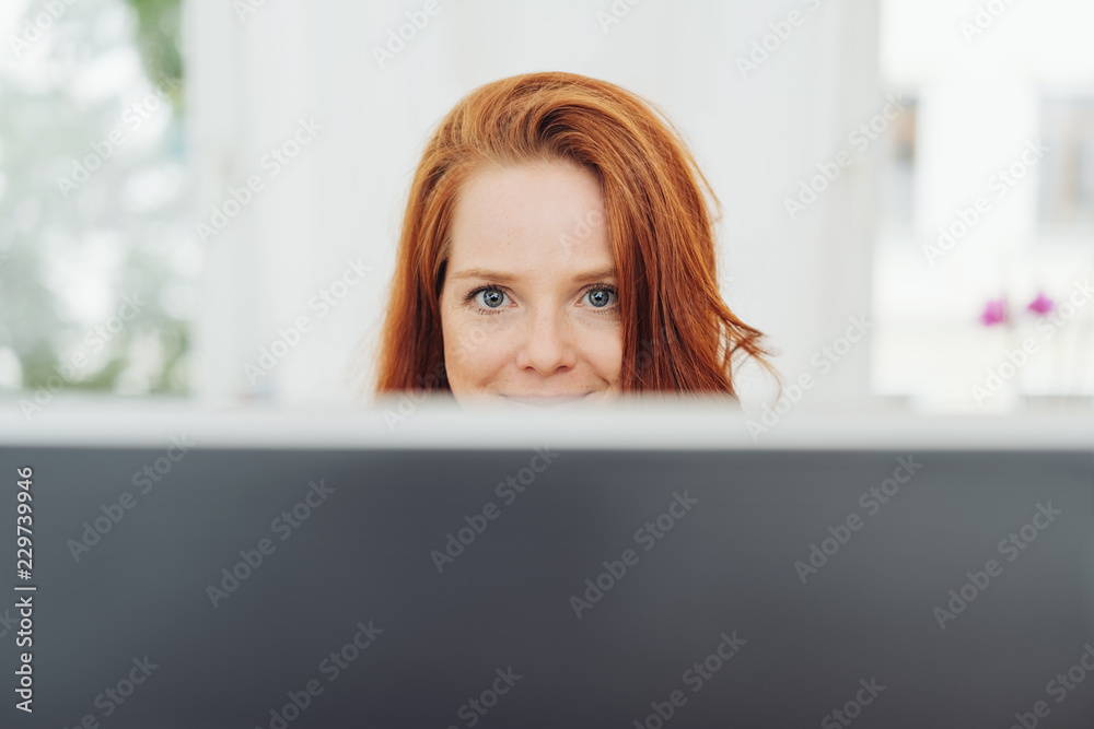 Smiling young businesswoman looking over a monitor Smiling young businesswoman looking over a monitor