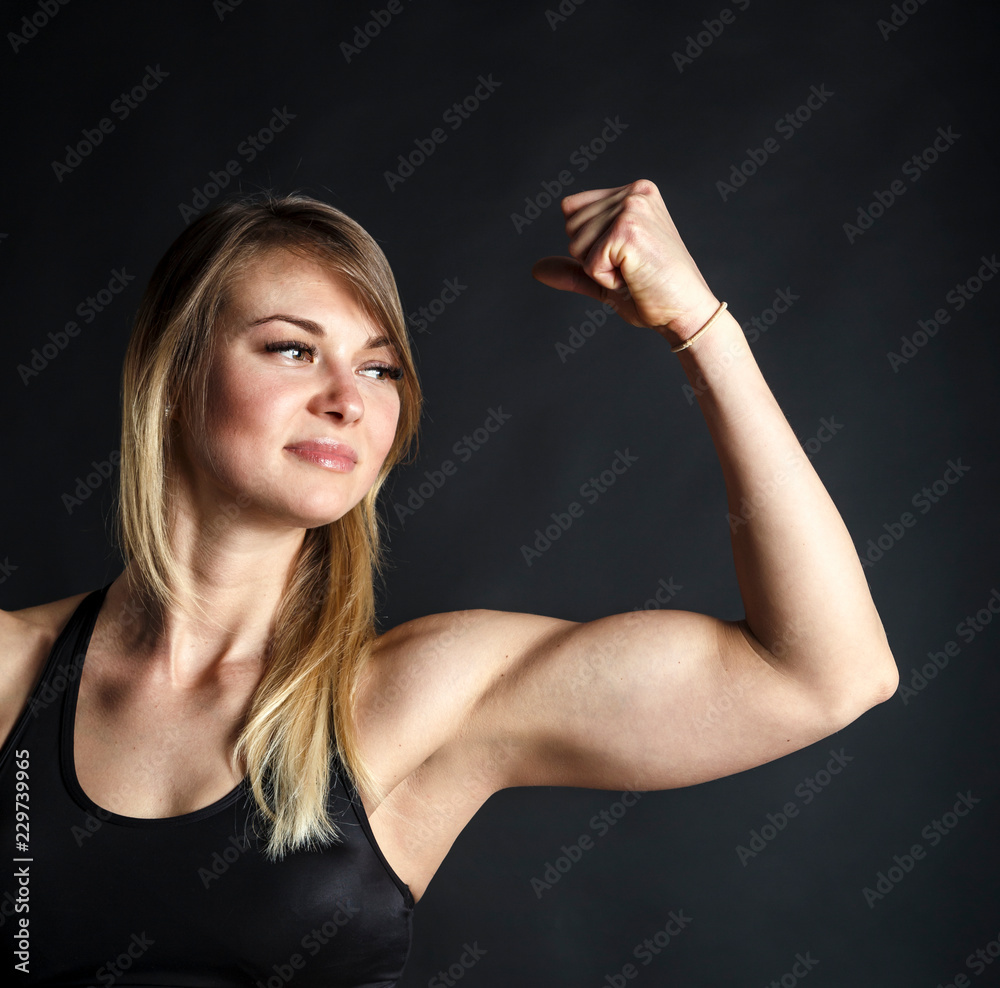 Attractive fitness woman is showing her biceps on black background