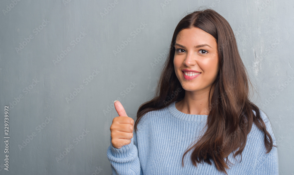 Young brunette woman over grunge grey wall happy with big smile doing ok sign, thumb up with fingers, excellent sign Young brunette woman over grunge grey wall happy with big smile doing ok sign, thumb up with fingers, excellent sign