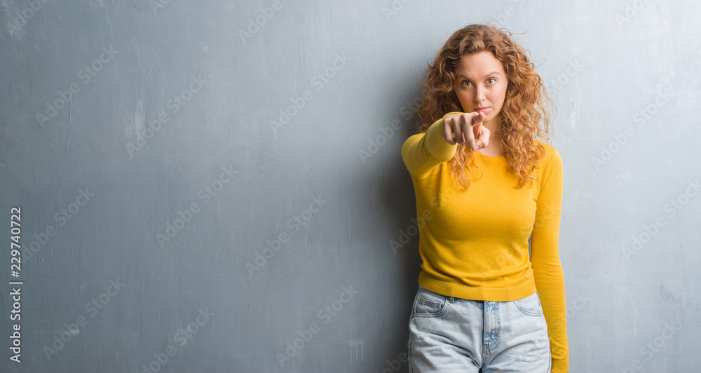 Young redhead woman over grey grunge wall pointing with finger to the camera and to you, hand sign, positive and confident gesture from the front Young redhead woman over grey grunge wall pointing with finger to the camera and to you, hand sign, positive and confident gesture from the front