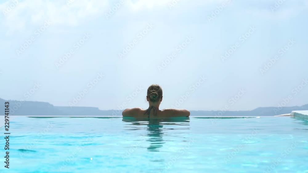 Young woman relaxing in the pool with a gorgeous view on Santorini Young woman relaxing in the pool with a gorgeous view on Santorini
