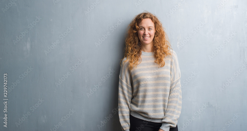 Young redhead woman over grey grunge wall with a happy and cool smile on face. Lucky person.