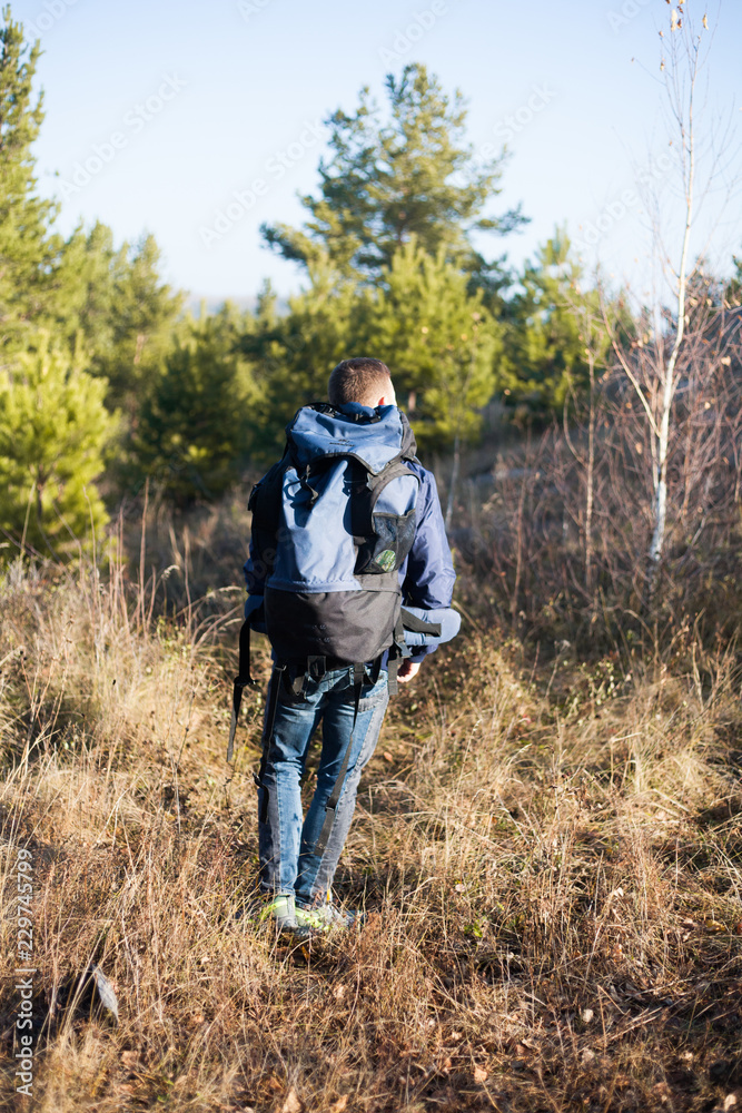 handsome man guy tourist standing alone by the mountain forest landscape during his summer vacation with his backpack back view