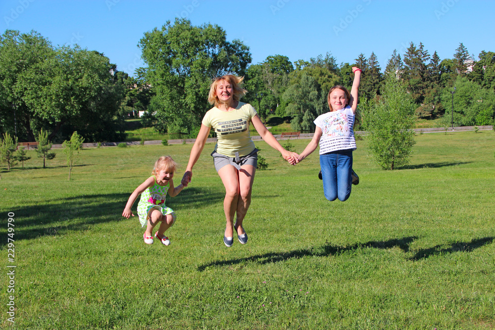 Obraz premium Happy mother having fun jumping with her daughters on green grass