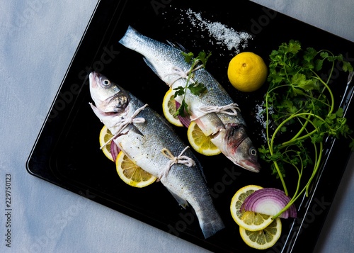 Two branzino fish stuffed with herbs, onion and lemon slices on a baking tray photo