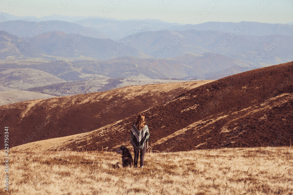 Obraz premium A girl in an authentic poncho with a green pattern play with husky. Ukrainian Carpathians in autumn time. Warm colored green leaves.Forests and mountains top view. Travel with dog.